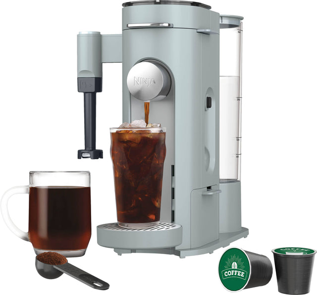 The image features a coffee machine, which is likely a Ninja Coffee Bar, sitting on a counter. The coffee machine is filled with coffee and has a cup of coffee on the side. There is also a spoon and a cup of tea nearby. The scene suggests a cozy and inviting atmosphere for enjoying a hot beverage.